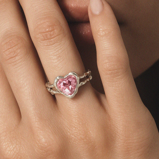Close-up of pink heart crystal ring on hand with textured silver band
